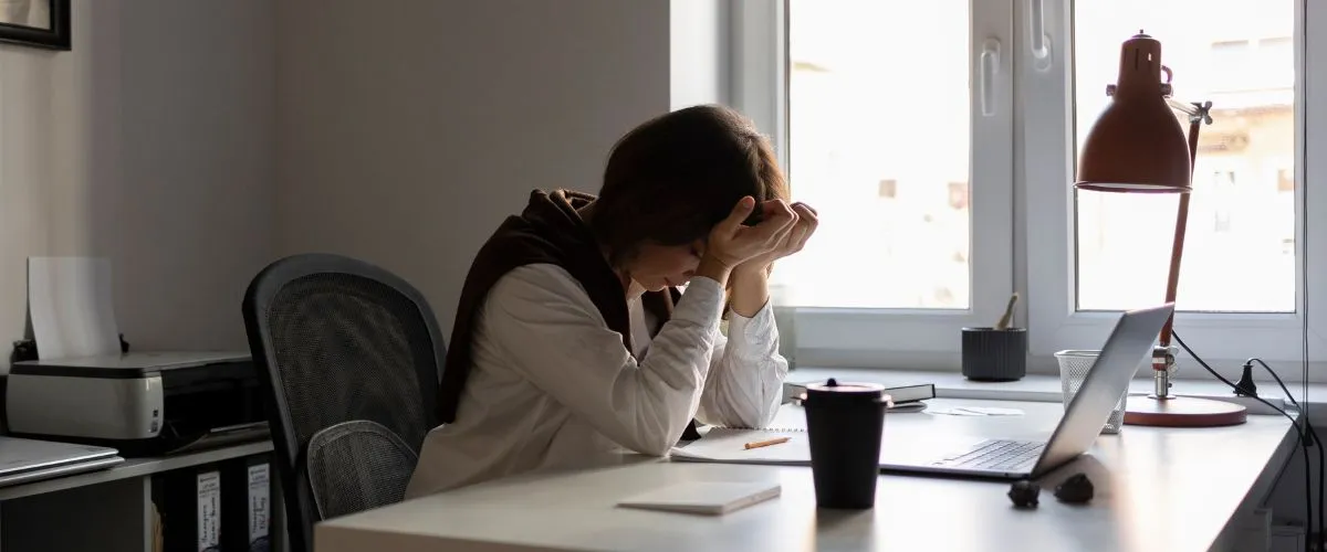 Employee sitting at a desk looking exhausted while reflecting on burnout and depression